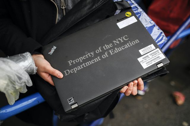 A photo of a hand holding a black laptop labelled Property of NYC Department of Education.